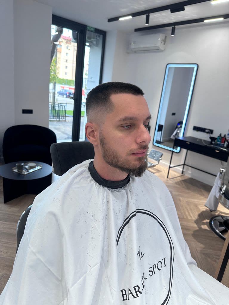Client proaspăt tuns, cu pelerina The Barber Spot, salonul în spate